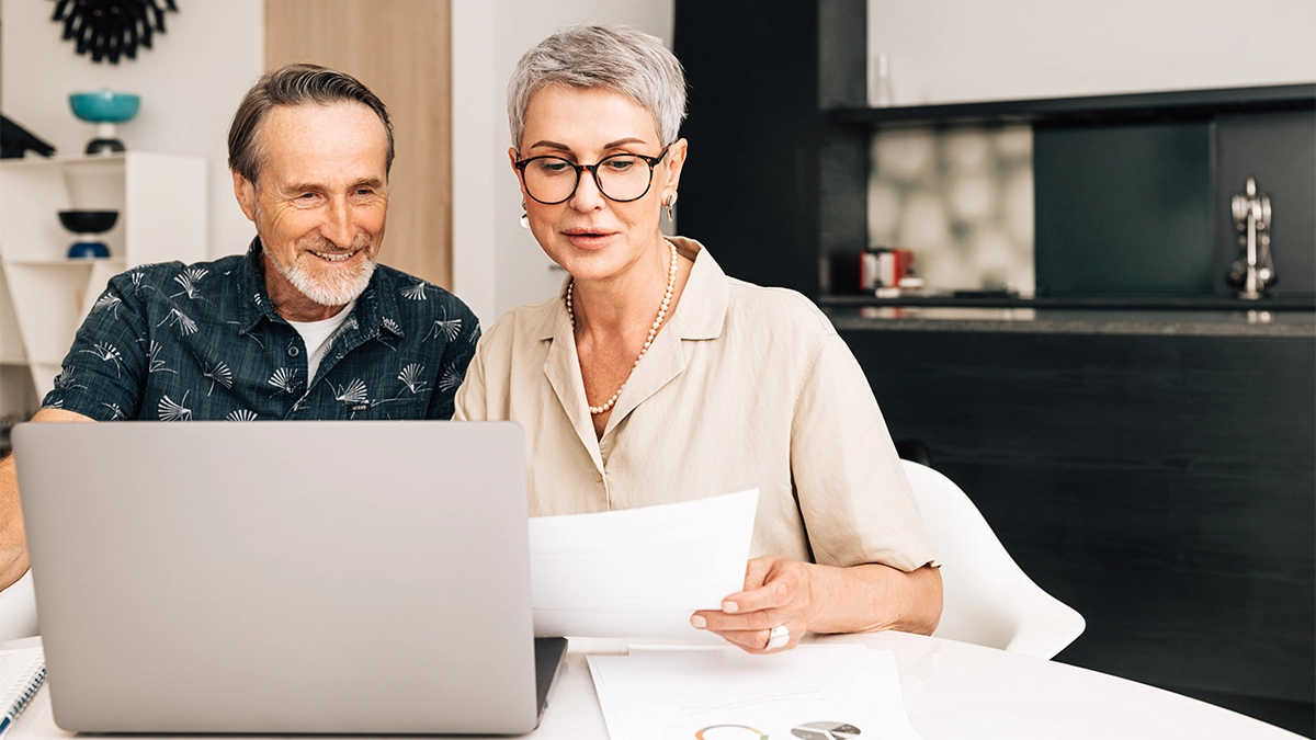Senior retired couple at a table in dining room using a laptop computer.